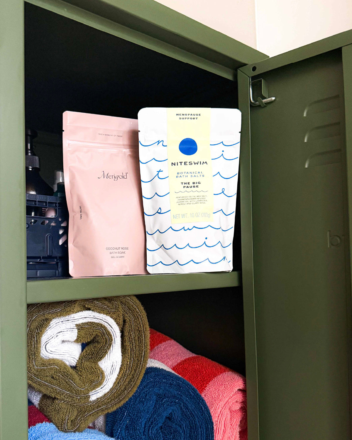 Big Pause bath salts pouch beside a pink bath salts pouch in an olive green locker