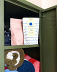 Big Pause bath salts pouch beside a pink bath salts pouch in an olive green locker