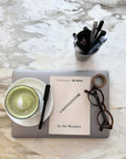In the Margins journal on a laptop beside a matcha latte, glasses and pens on marble