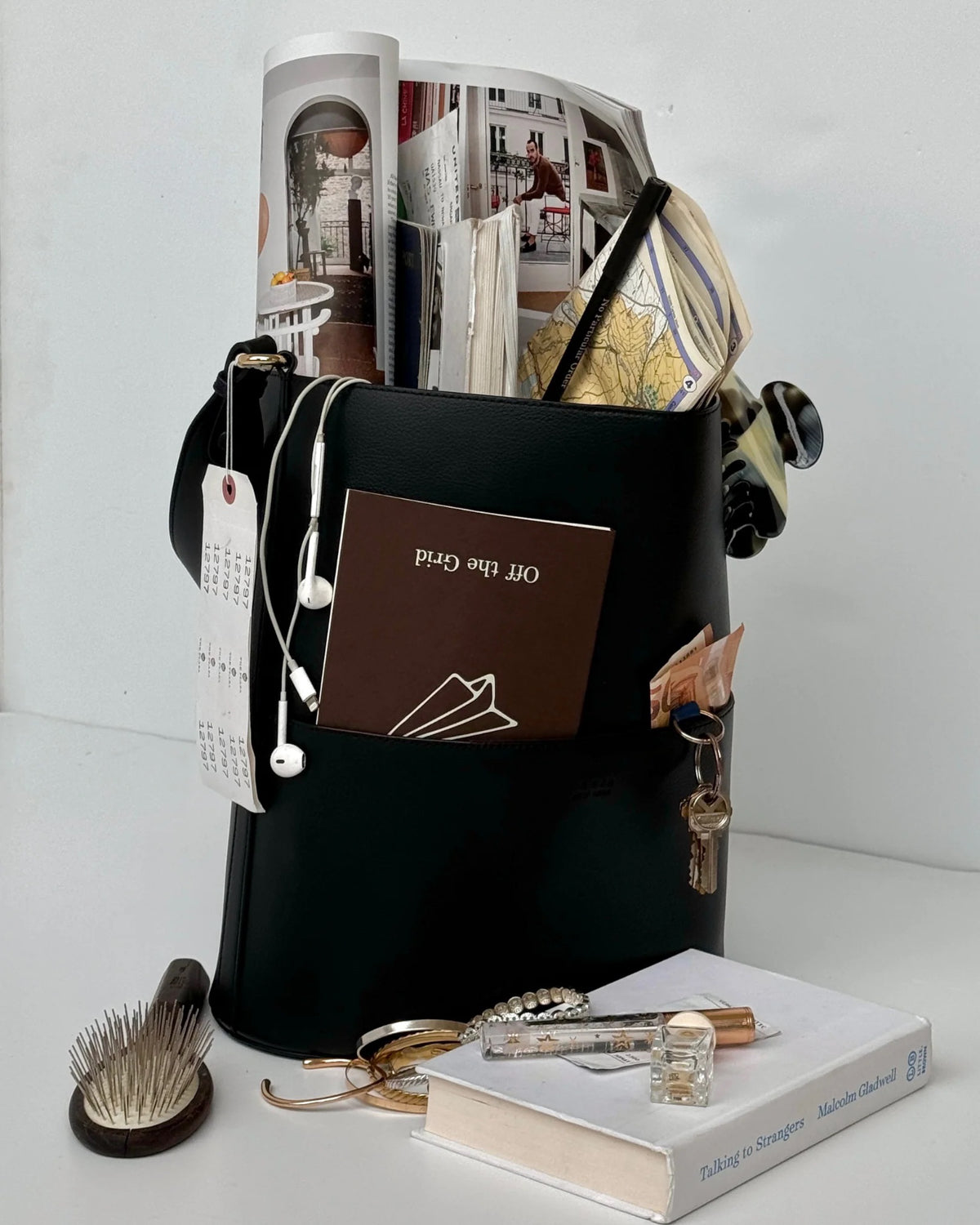 Off the Grid travel journal tucked in a black tote with earbuds, keys and a book