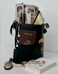 Off the Grid travel journal tucked in a black tote with earbuds, keys and a book