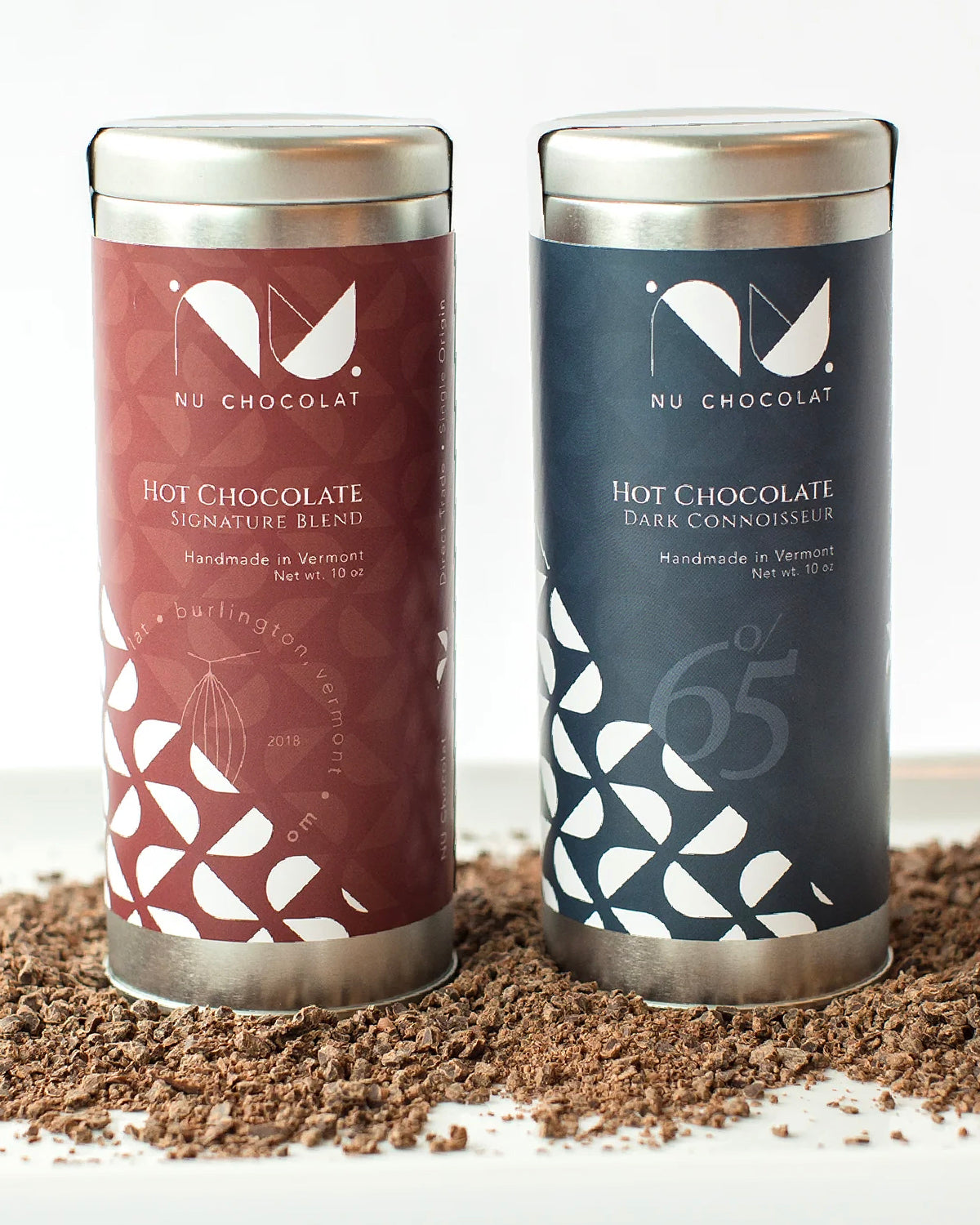 Nu Chocolat Signature Blend and 65% Dark hot chocolate tins on chocolate shavings