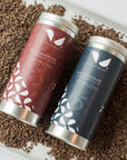 Overhead view of two Nu Chocolat hot chocolate tins surrounded by shaved chocolate