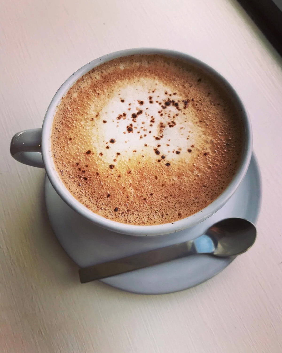 Cup of frothy hot chocolate on a gray saucer with a spoon