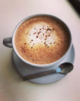 Cup of frothy hot chocolate on a gray saucer with a spoon
