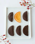 Nu Chocolat dark chocolate covered candied Italian orange segments on a white tray, one cut open, with red berries