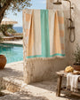 Colorful Turkish cotton towel hanging on an outdoor shower with a pool and garden in the background