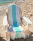 Beach chair with a Turkish cotton towel draped over it on a sandy beach.