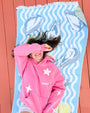 Person wearing a pink hoodie, lying on a blue Turkish towel with oyster design against a red wooden background.