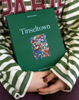 Person in a striped sweater hugging the green Tinseltown 1000-piece puzzle box