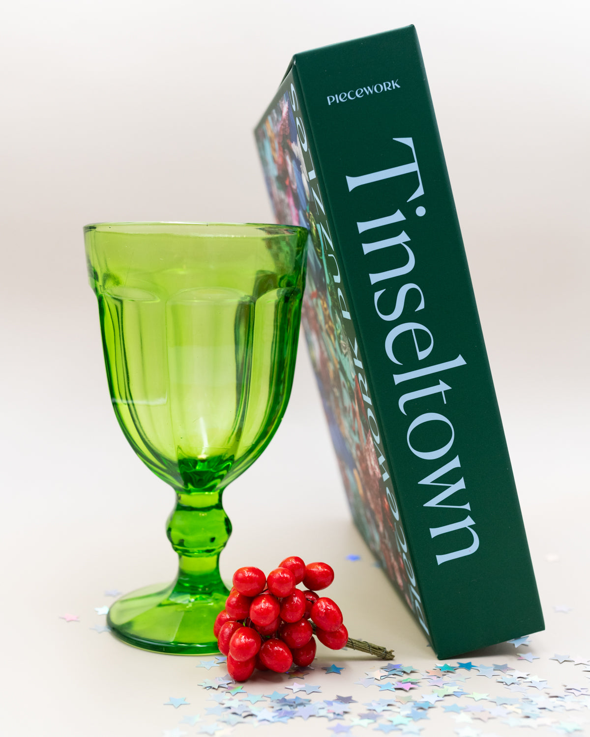 Tinseltown puzzle box standing beside a green glass goblet and red berries