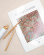 William Morris Florals coloring book with a pink floral cover beside colored pencils