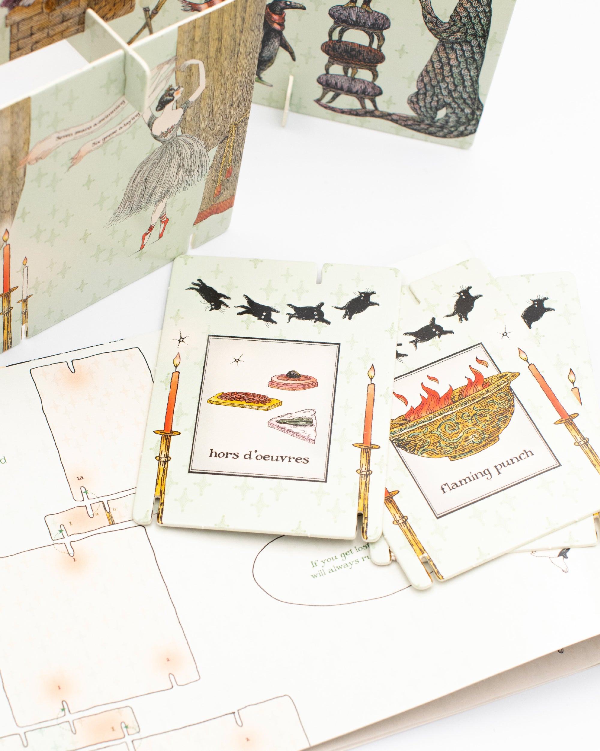 Close up of cards from Edward Gorey's Eclectic Decor holiday tabletop craft featuring an illustration of hors d'oeuvres and flaming punch.