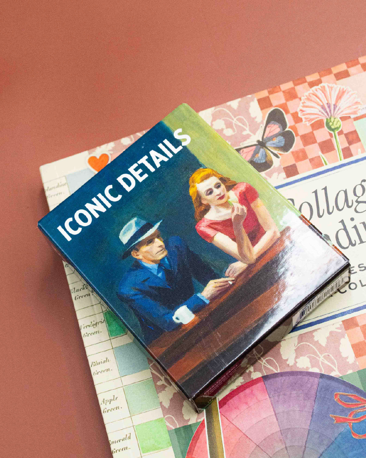 Iconic Details art quiz deck box with a painted diner couple on the cover, on a red desk