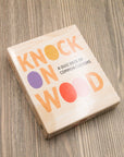 Knock on Wood card deck box with peach and purple lettering on a wood table