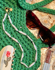 Green crocheted bag with sunglasses and lip balm on a textured surface