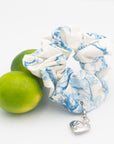 toile scrunchie with silver locket charm next to limes