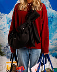 Woman wearing a black bow crossbody bag with a red sweater and jeans, styled for winter errands.