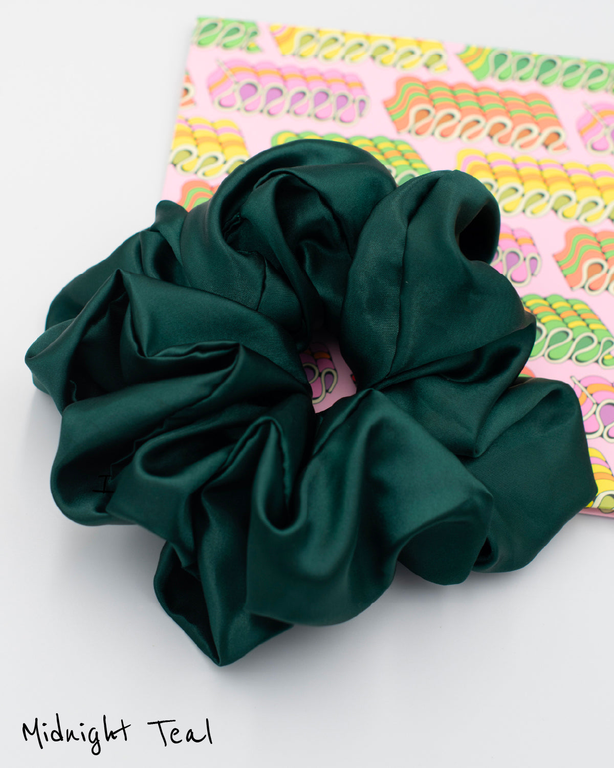 Midnight teal oversized satin scrunchie on decorative paper featuring pink, green and yellow vintage ribbon candies.
