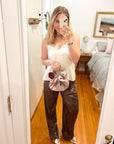 Woman wearing champagne satin rosette clutch bag with brown sequin pants and white silk top.