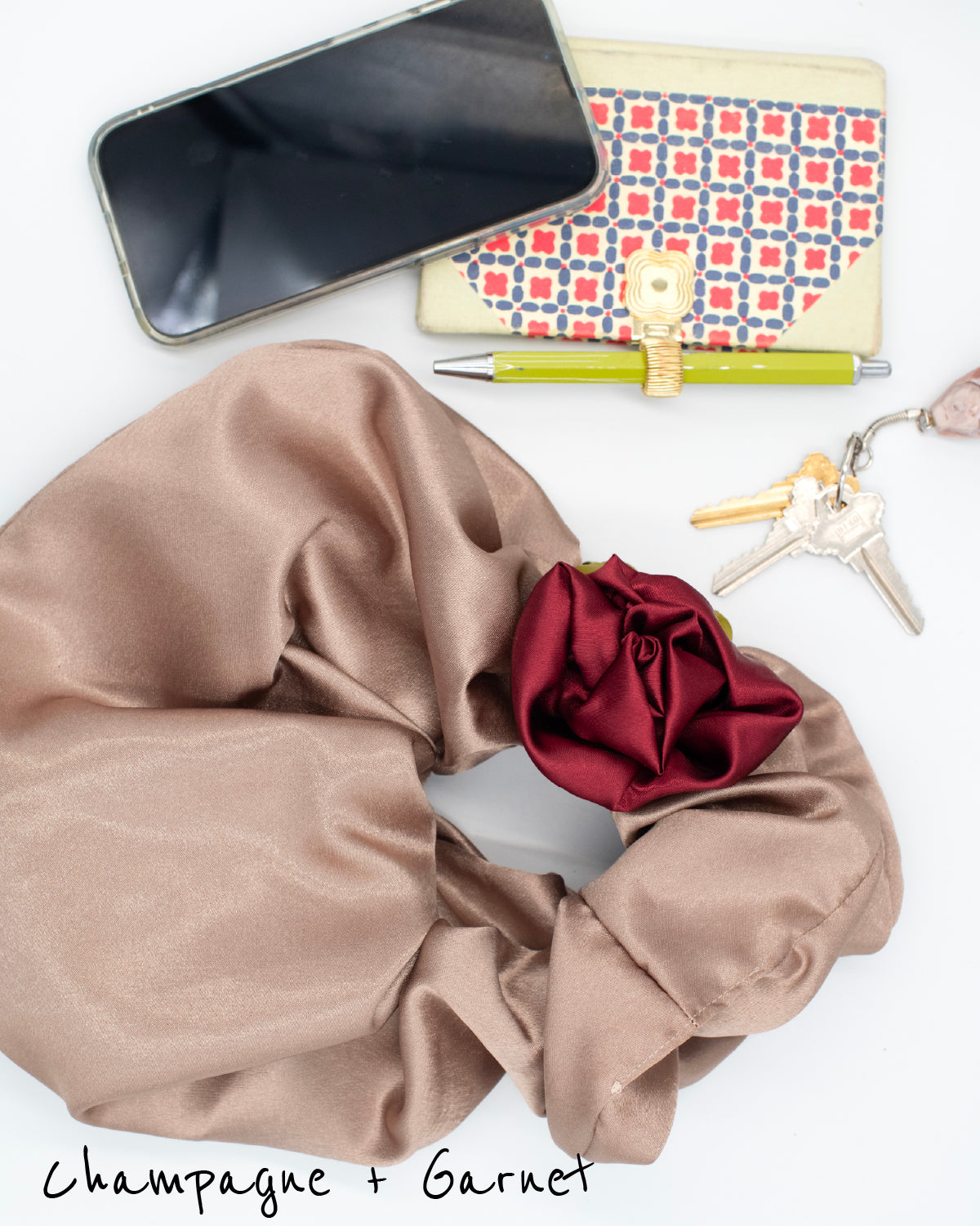 Champagne satin rosette clutch with garnet red hair tie, styled with wallet, keys, and lipstick.
