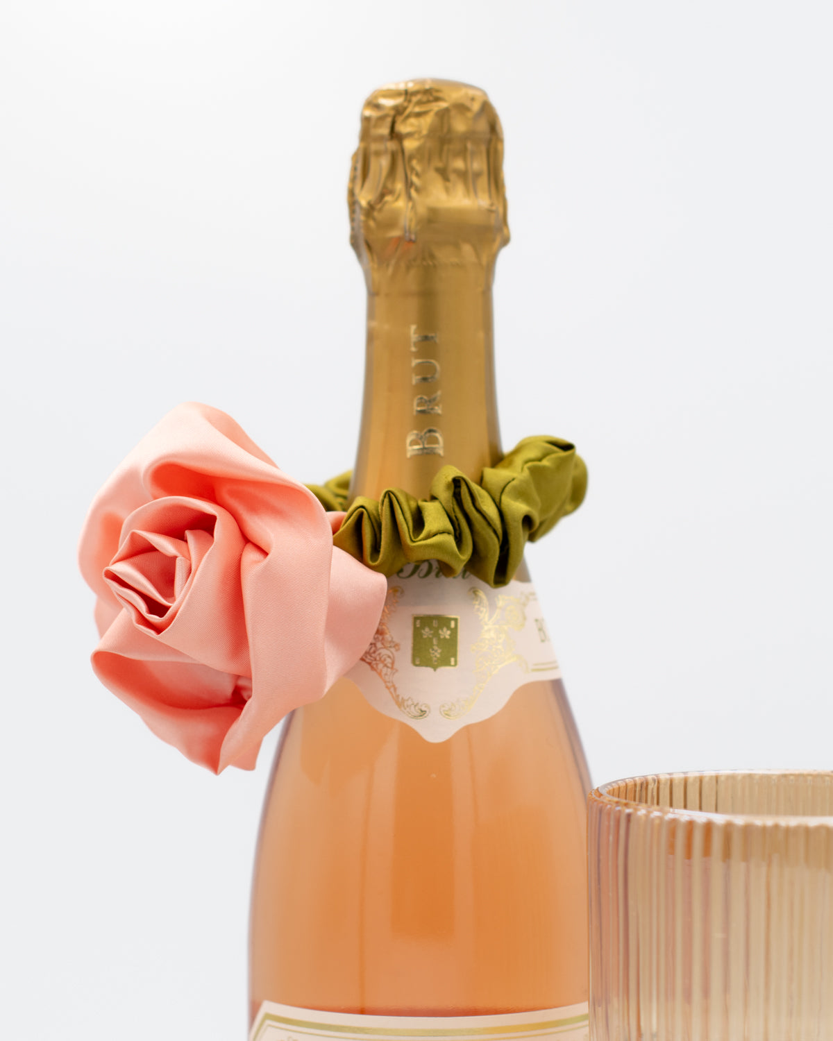 Neck of a champagne bottle with satin rosette scrunchie on a white background