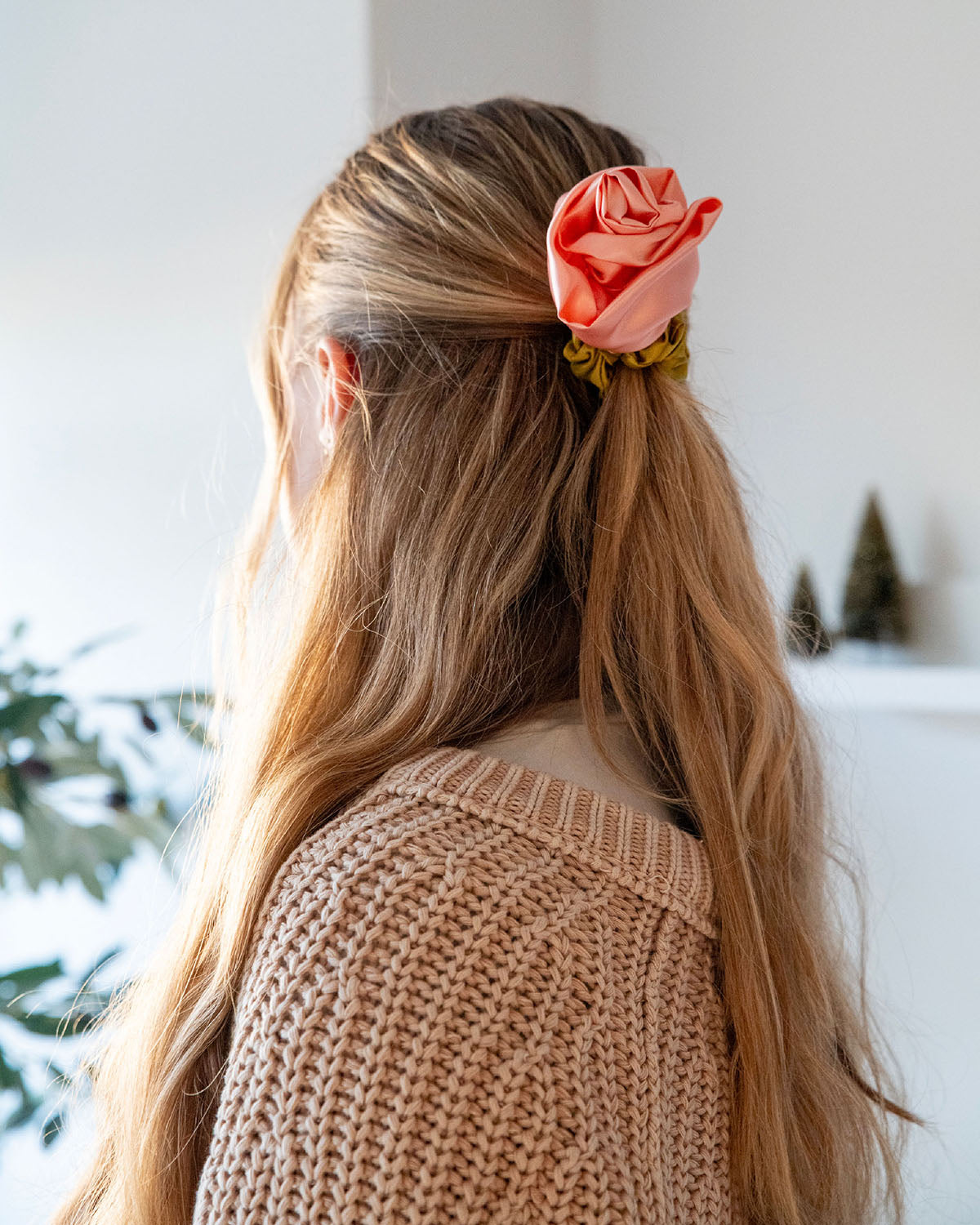 Back of a woman wearing a peach satin rosette scrunchie in a half ponytail with a beige sweater