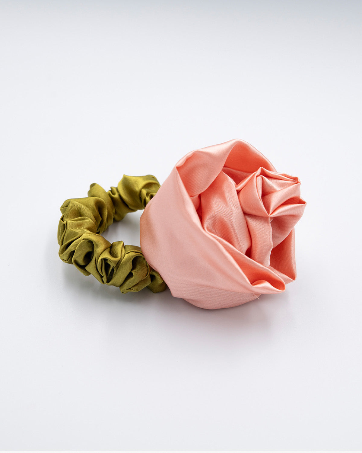 Satin peach colored rosette scrunchie with a cerulian green band, laying flat on a white background
