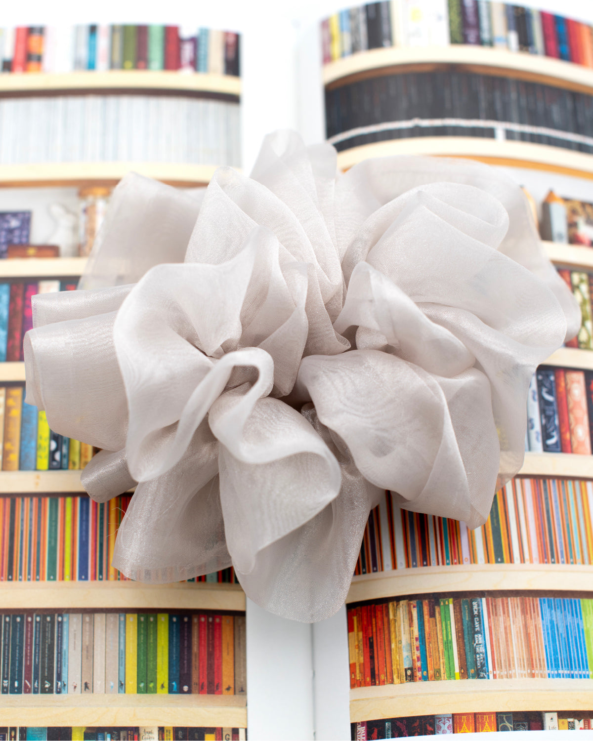 Oversized cloud colored hair scrunchie on top of an open book featuring image of colorful bookshelves.