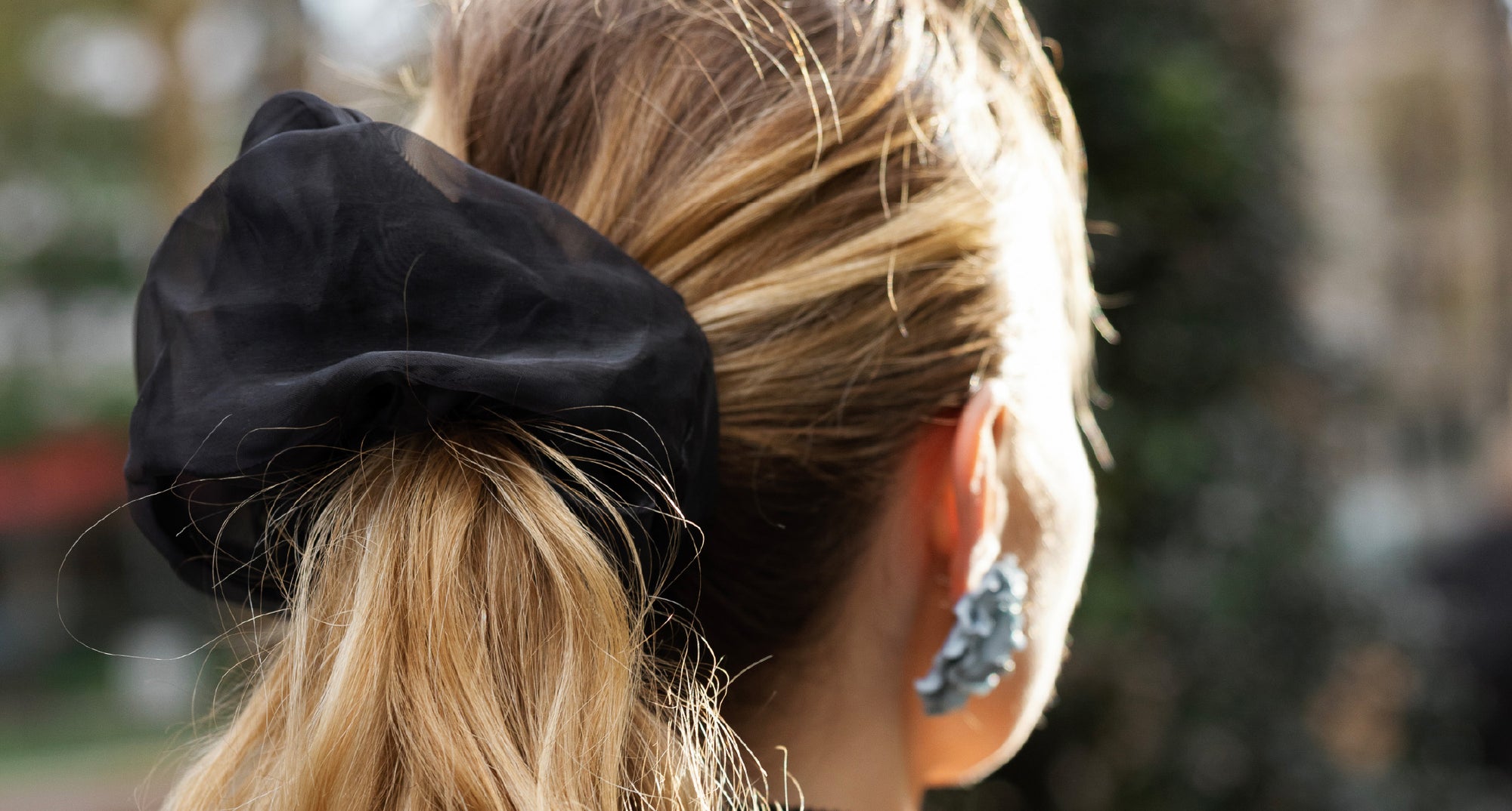 Close-up of a person with a black scrunchie in their hair, wearing blue earrings.