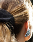 Close-up of a person with a black scrunchie in their hair, wearing blue earrings.