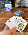 Hand holding a fan of Ski House Games cards with the blue box and deck on a wood table