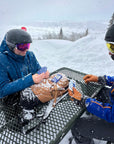 Two skiers playing cards on a snowy picnic table at a ski resort