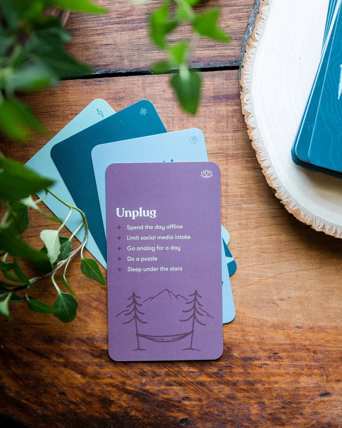 Plum Unplug card from the self-care deck fanned with blue cards on a wood table