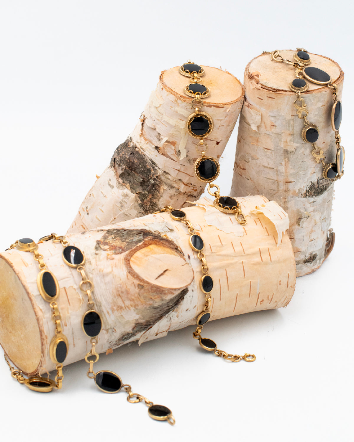 5 Vintage gold-filled bracelets with black onyx cabochons draped over 3 birch logs for a natural, styled jewelry display