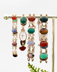 A collection of four antique gold-fill scarab bracelets with varying sizes, link styles, multi-colored stones and etchings on a jewelry display