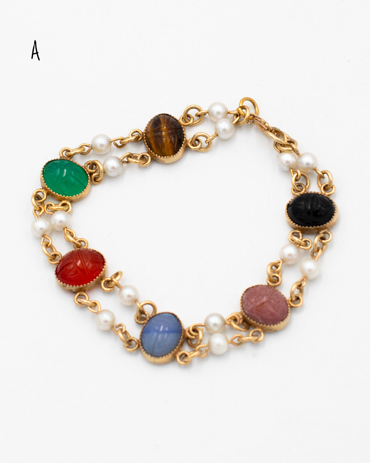Vintage scarab bracelet with double pearl links and multi-colored carved stones laying flat on a white background