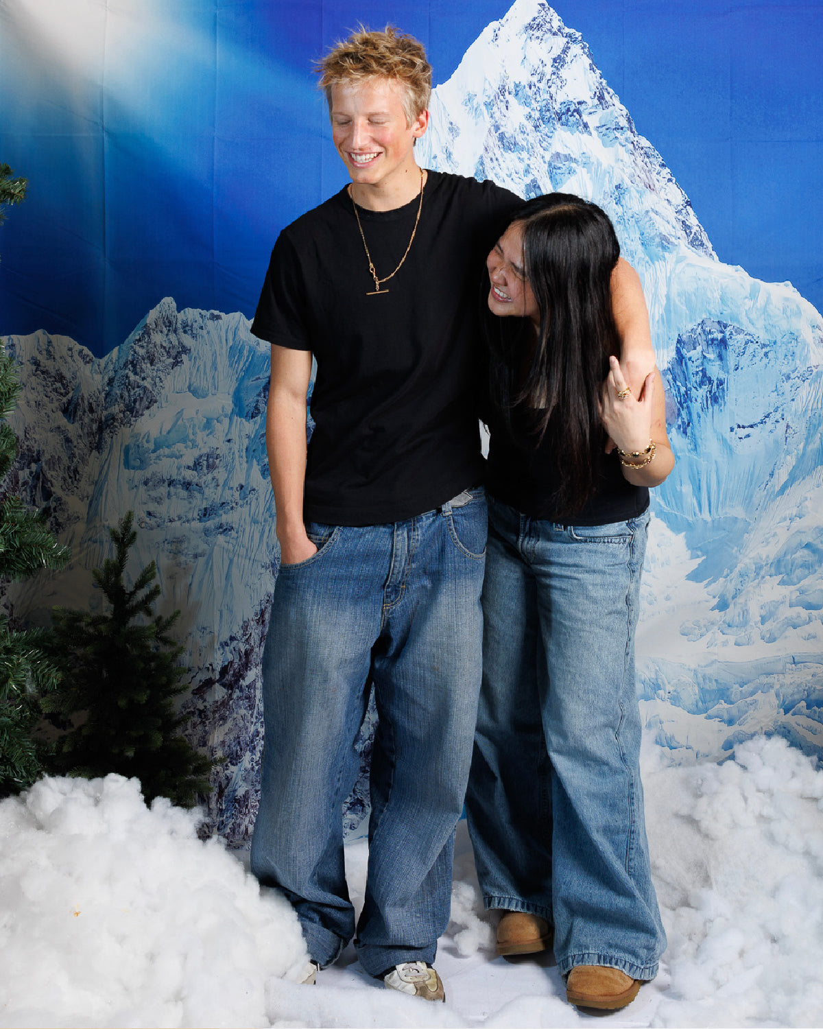 Male and female couple in black shirts and jeans, standing against a faux wintry backdrop, wearing necklaces made from Victorian-era men’s watch chains with antique T-bars and dog clips. Authentic 100+ year-old pieces made from sustainable vintage chains