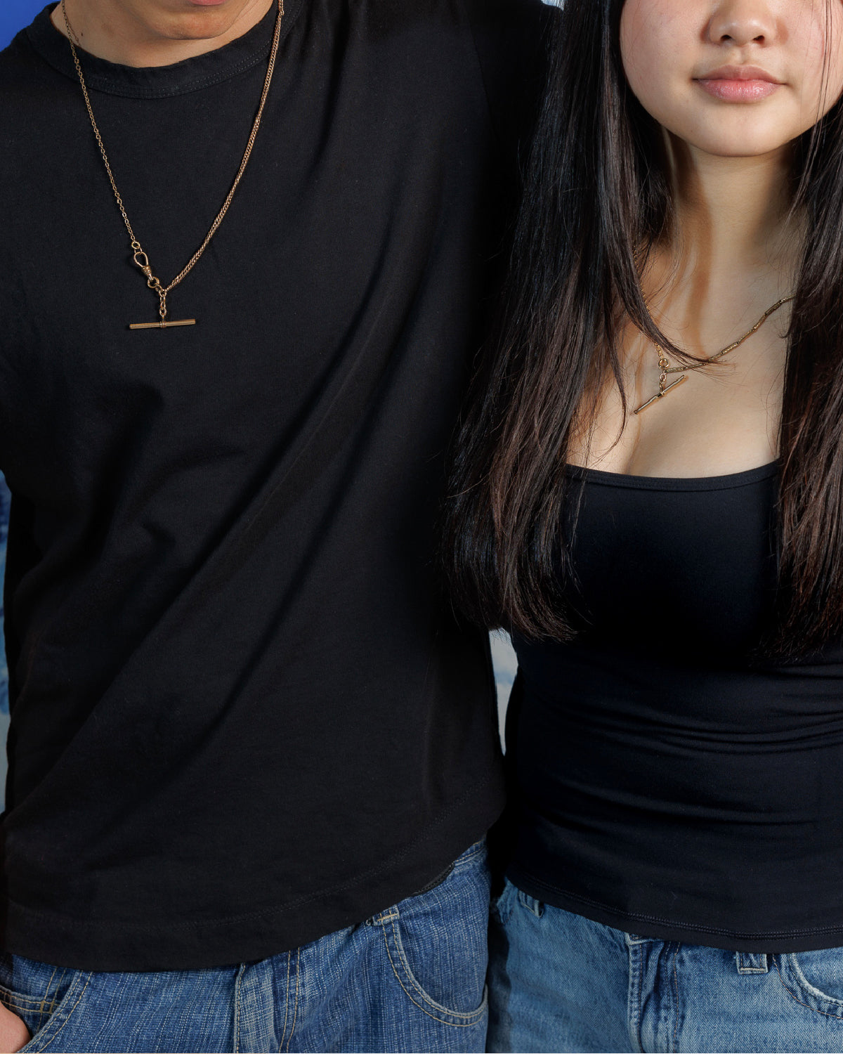 Close up of man and woman in black shirts and blue jeans wearing necklaces made with antique Victorian watch chains with t-bars and dog clips.