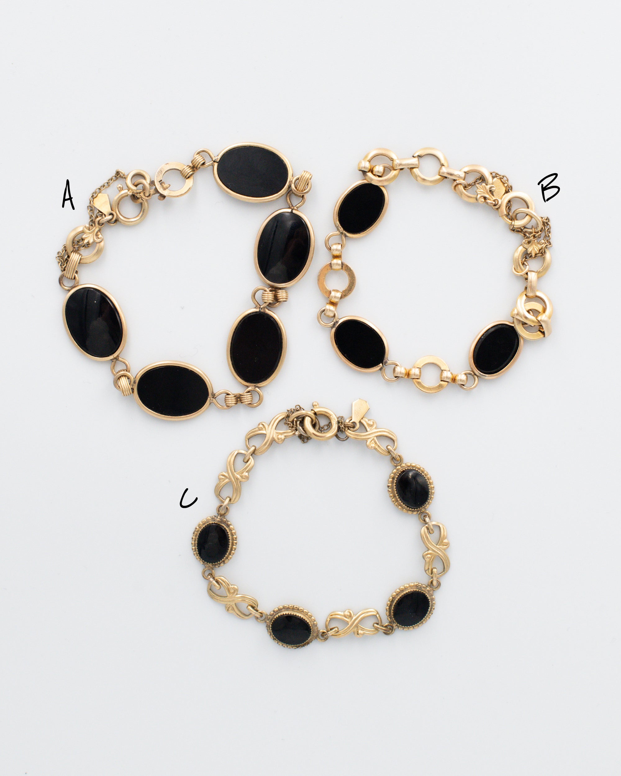 Vintage AMCO black onyx gold-filled bracelets displayed flat on a white background, featuring three sizes with polished onyx stones and detailed gold-fill links, each with an attached chain guard.