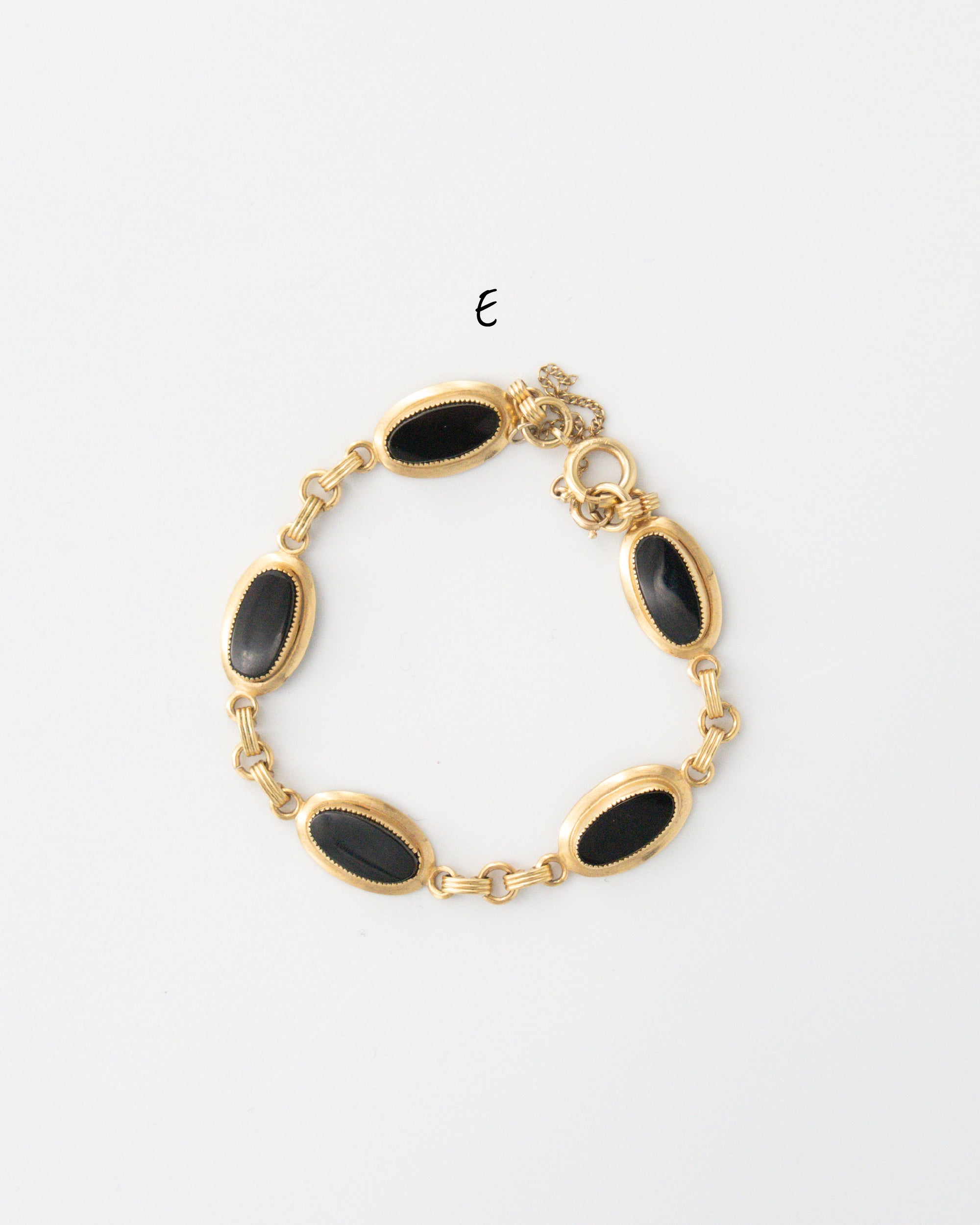 Vintage gold-filled bracelet with five polished oval black onyx cabochons set in thick bezels with a chainguard, shown flat on a white background.