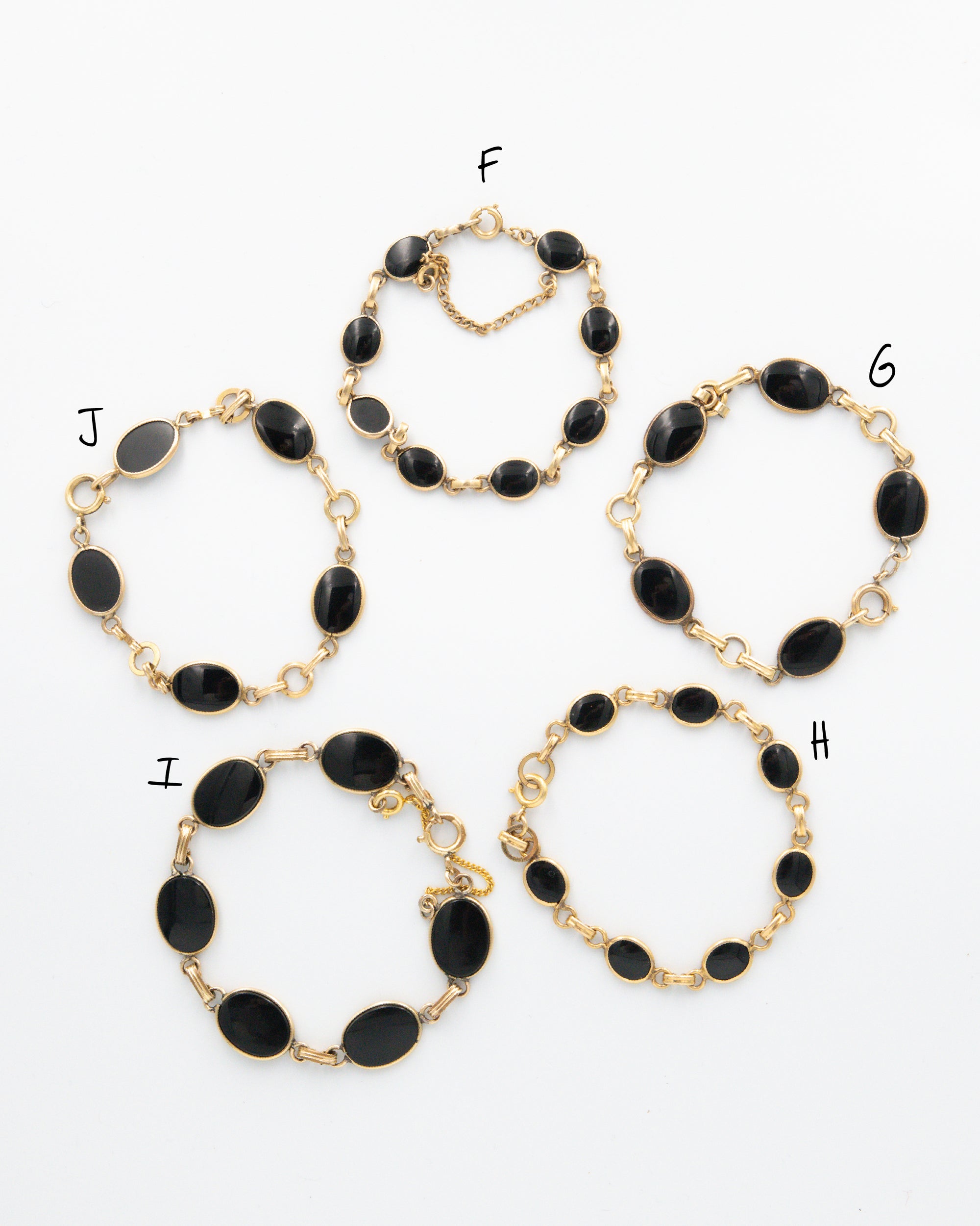 A collection of vintage onyx bracelets set and linked in 12K gold-fill laying flat on a white background.