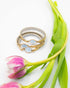 A glowing glass moonstone link set on a stretch, gold-fill band reclaimed from vintage timepieces, on a white background with pink flowers