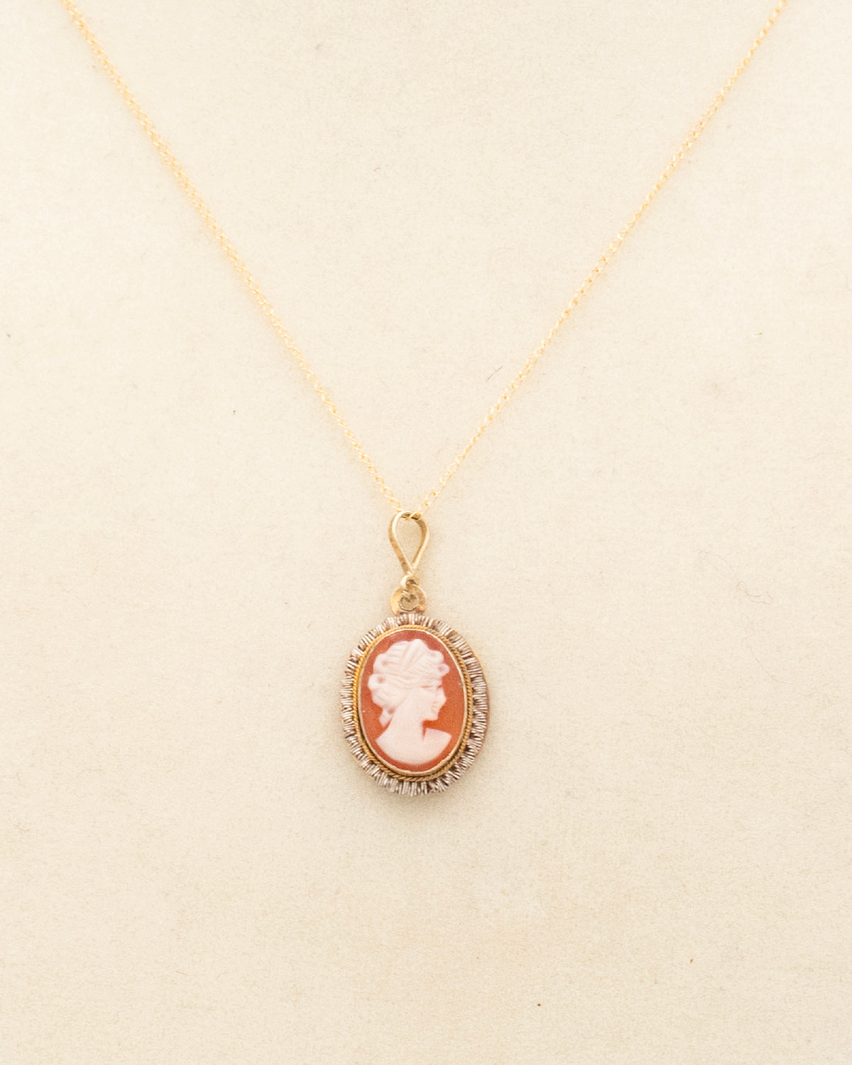 Close up of hand-carved shell cameo in ruffle-edge gold-filled setting from the 1950s-60s, displayed on beige background