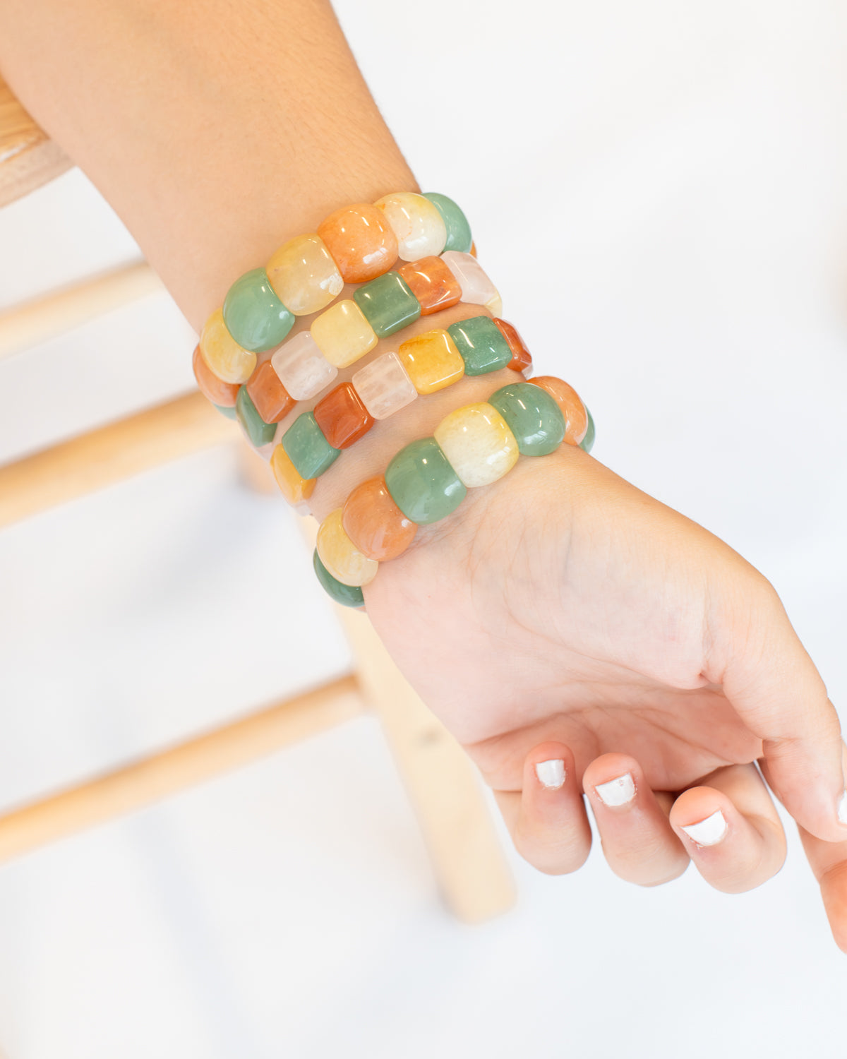 Close-up of a wrist wearing four stacked chicklet agate stone beaded bracelets in a mix of green, orange, yellow, and white stone beads.