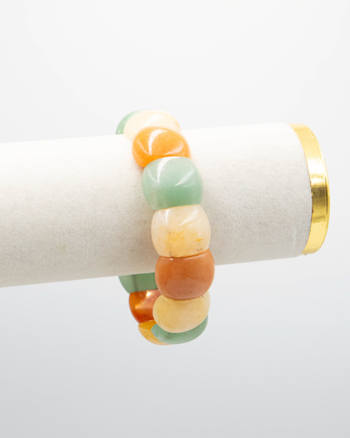 Chicklet agate stone bracelet with rounded multicolor beads in green, orange, and cream draped over a white jewelry display stand with a gold rim.