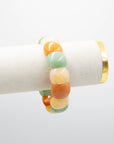 Chicklet agate stone bracelet with rounded multicolor beads in green, orange, and cream draped over a white jewelry display stand with a gold rim.