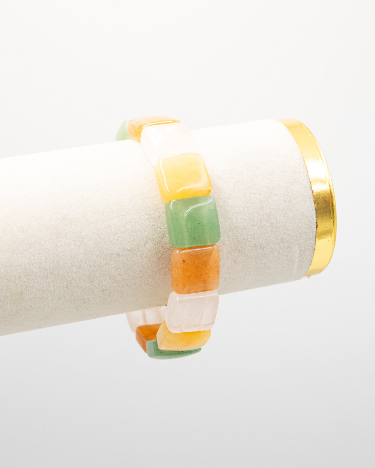 Chicklet agate stone bracelet with rounded multicolor beads in green, orange, and cream draped over a white jewelry display stand with a gold rim.