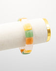 Chicklet agate stone bracelet with rounded multicolor beads in green, orange, and cream draped over a white jewelry display stand with a gold rim.