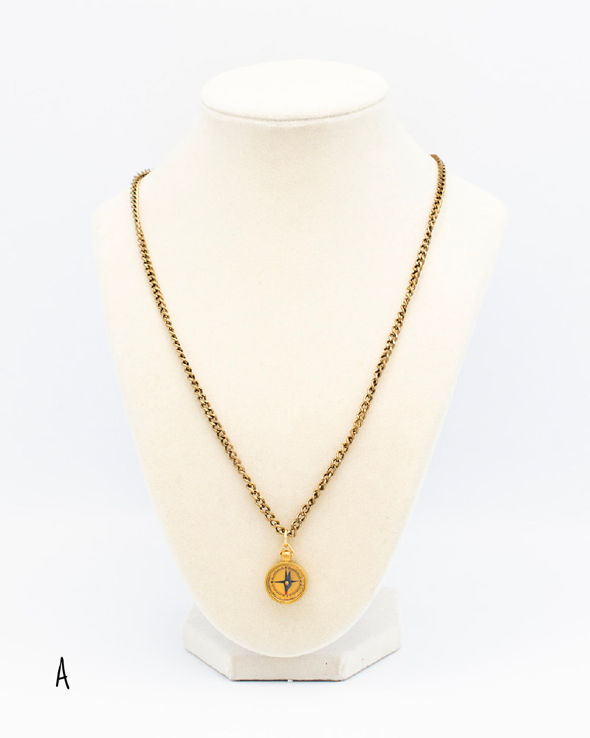 Vintage 1970s compass pendant on a brass chain draped on a jewelry bust